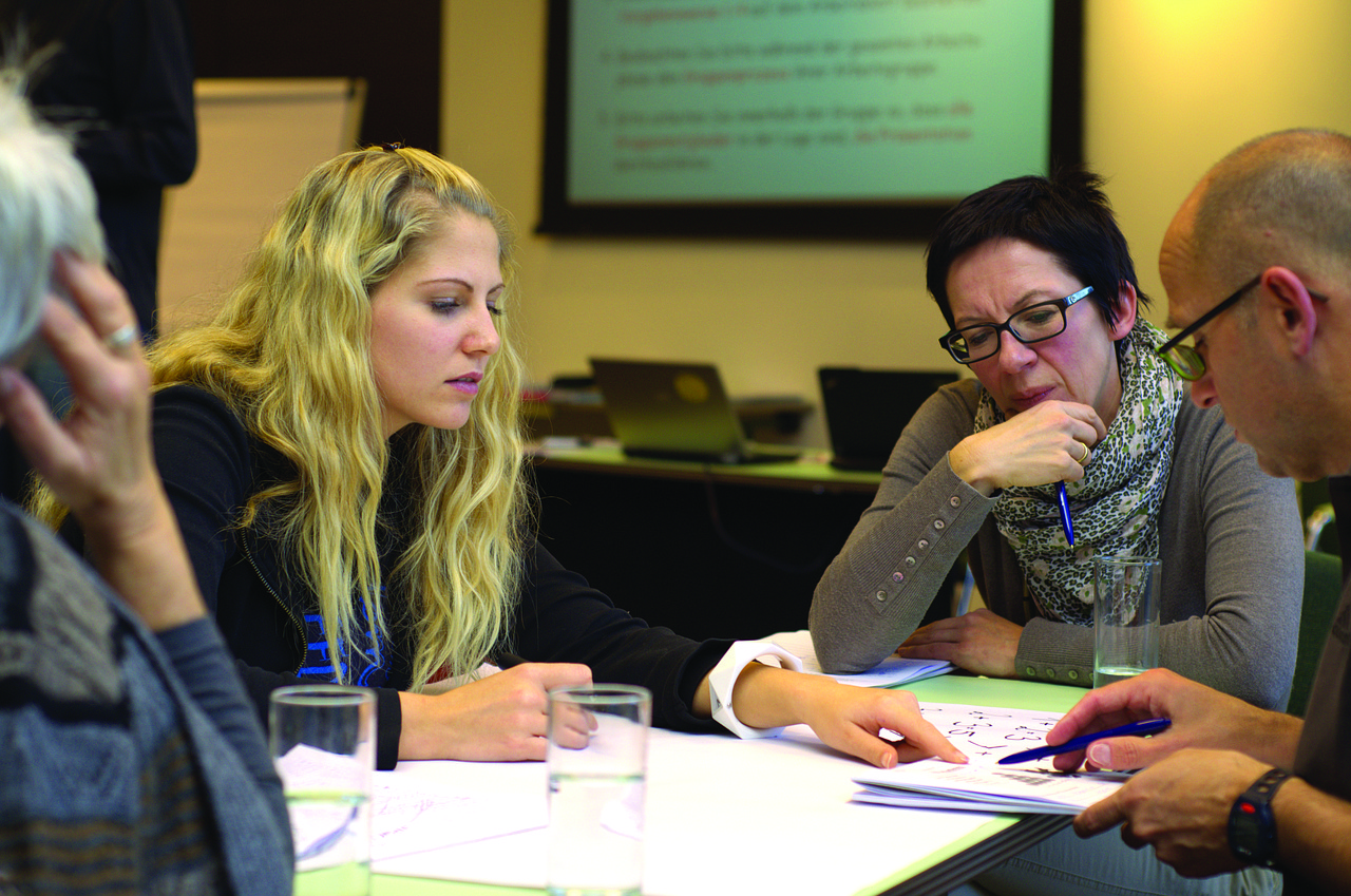 A professional team discussing work priorities in a sunlit meeting space