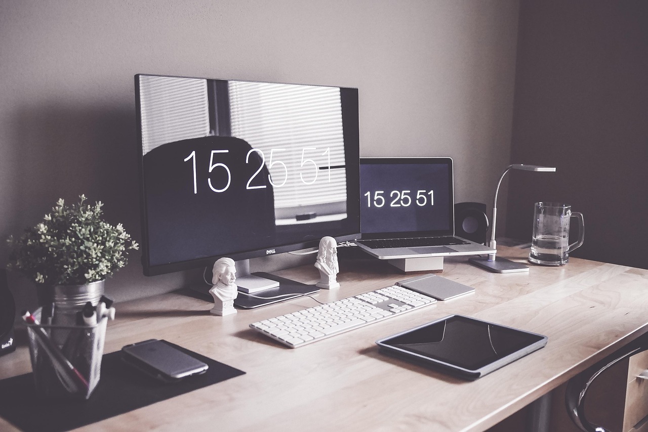 A remote employee reviewing documents on a desk with dual monitors in a home office.