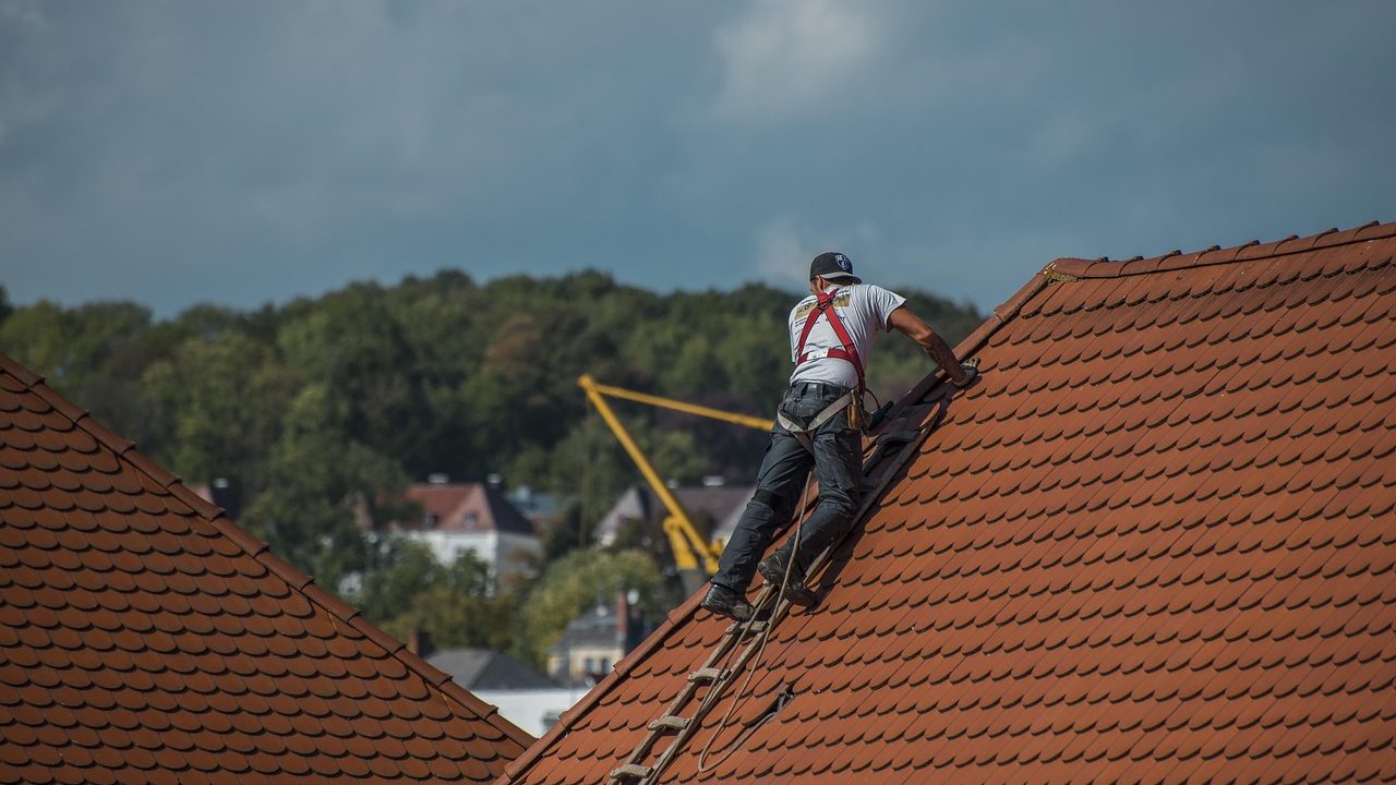 Roofing professional inspecting an open metal roof valley on an asphalt shingle roof.