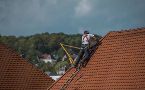 Roofing professional inspecting an open metal roof valley on an asphalt shingle roof.