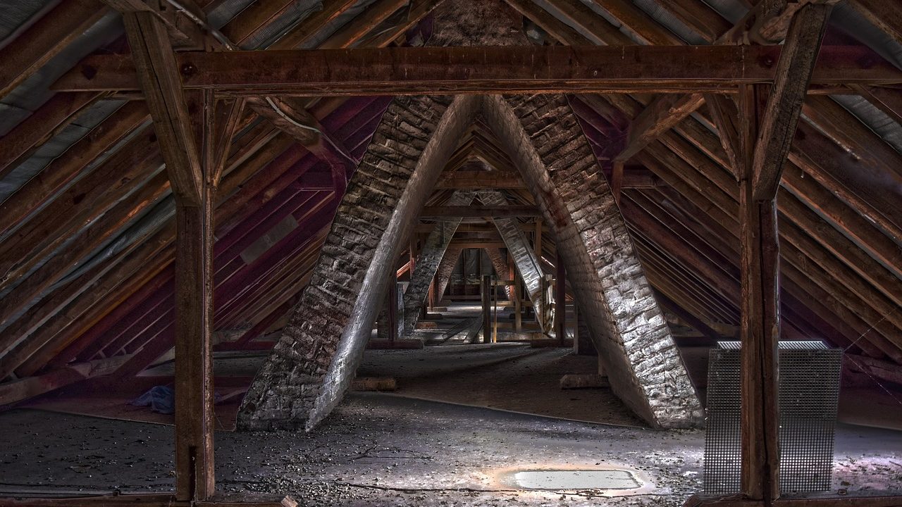 Attic interior showing reflective radiant barrier foil on roof rafters alongside thick loose-fill blown insulation on the attic floor.