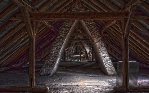 Attic interior showing reflective radiant barrier foil on roof rafters alongside thick loose-fill blown insulation on the attic floor.