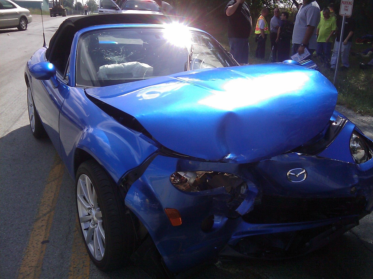 A parked sedan with rear bumper collision damage along a suburban curb.