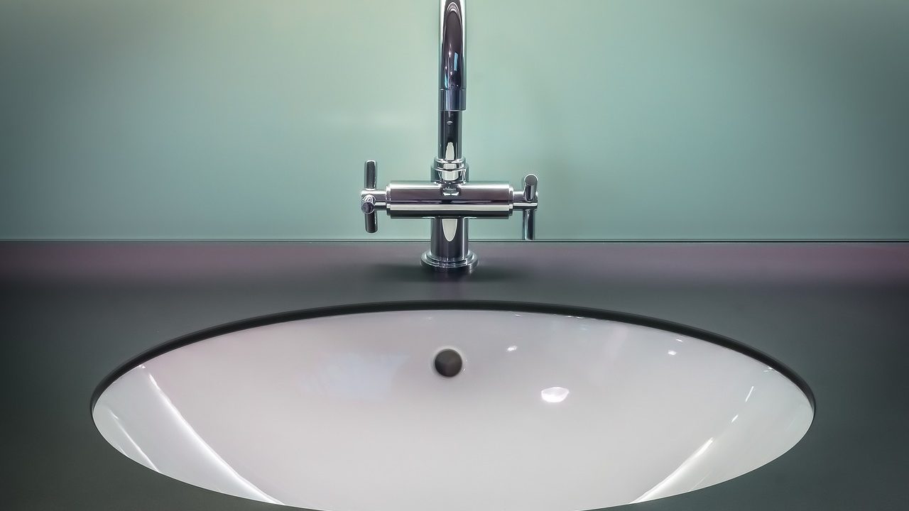 A home improver adjusting a metal pop-up sink linkage strap under a bathroom vanity drain pipe.