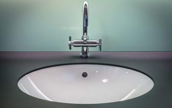 A home improver adjusting a metal pop-up sink linkage strap under a bathroom vanity drain pipe.