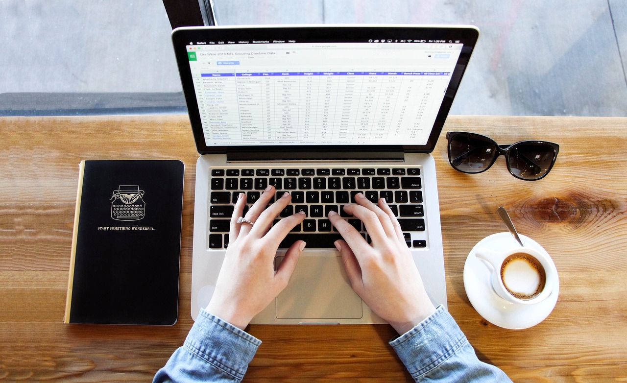 Hands typing on a laptop keyboard at an organized wooden desk.