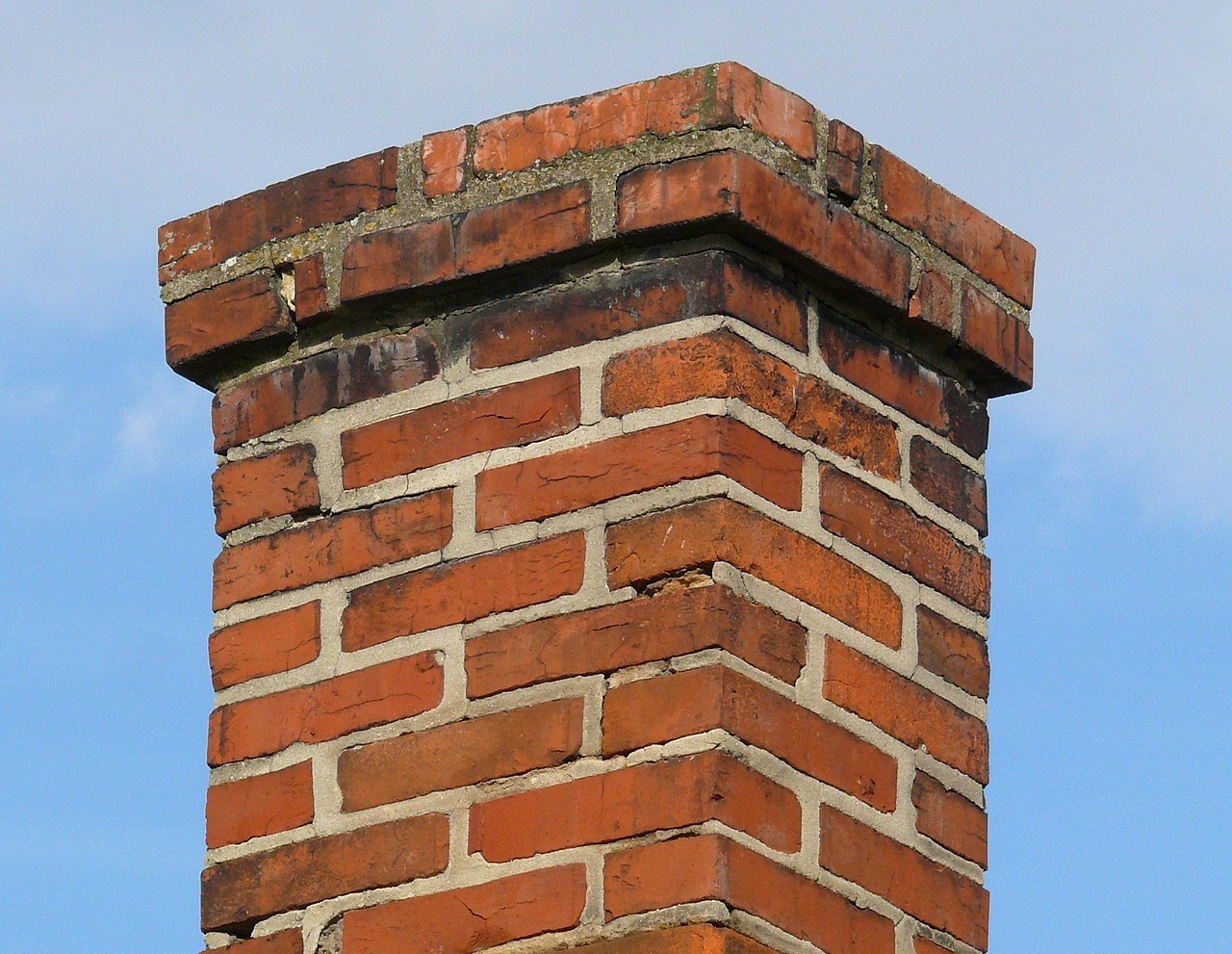 Contractor inspecting stepped metal flashing along a brick chimney roof junction.