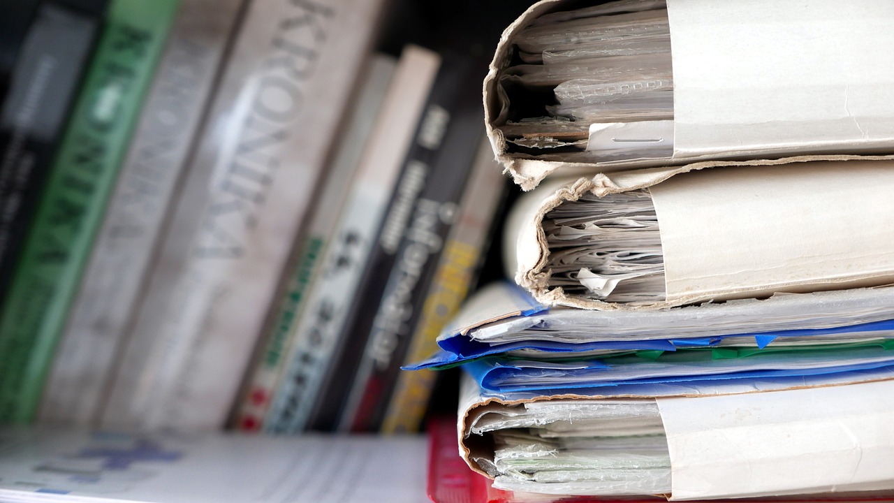 Close-up of written documentation and work records compiled on a desk next to a laptop.