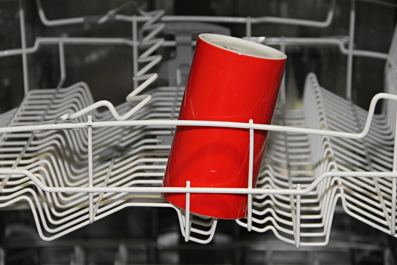 Close-up of a person arranging small plates and bowls inside a portable countertop dishwasher rack