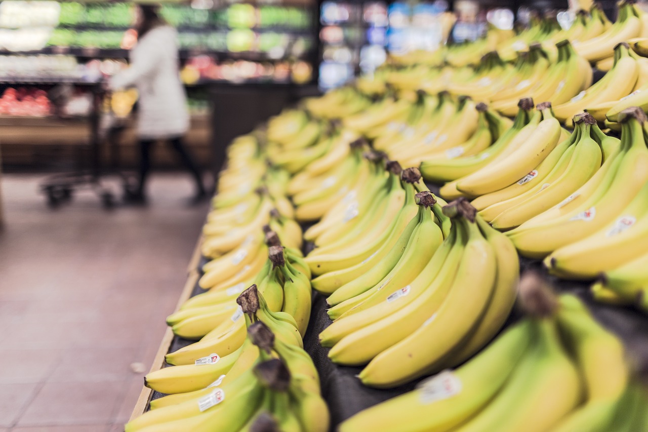 Shopper comparing food options on a grocery store aisle shelf under bright lighting.