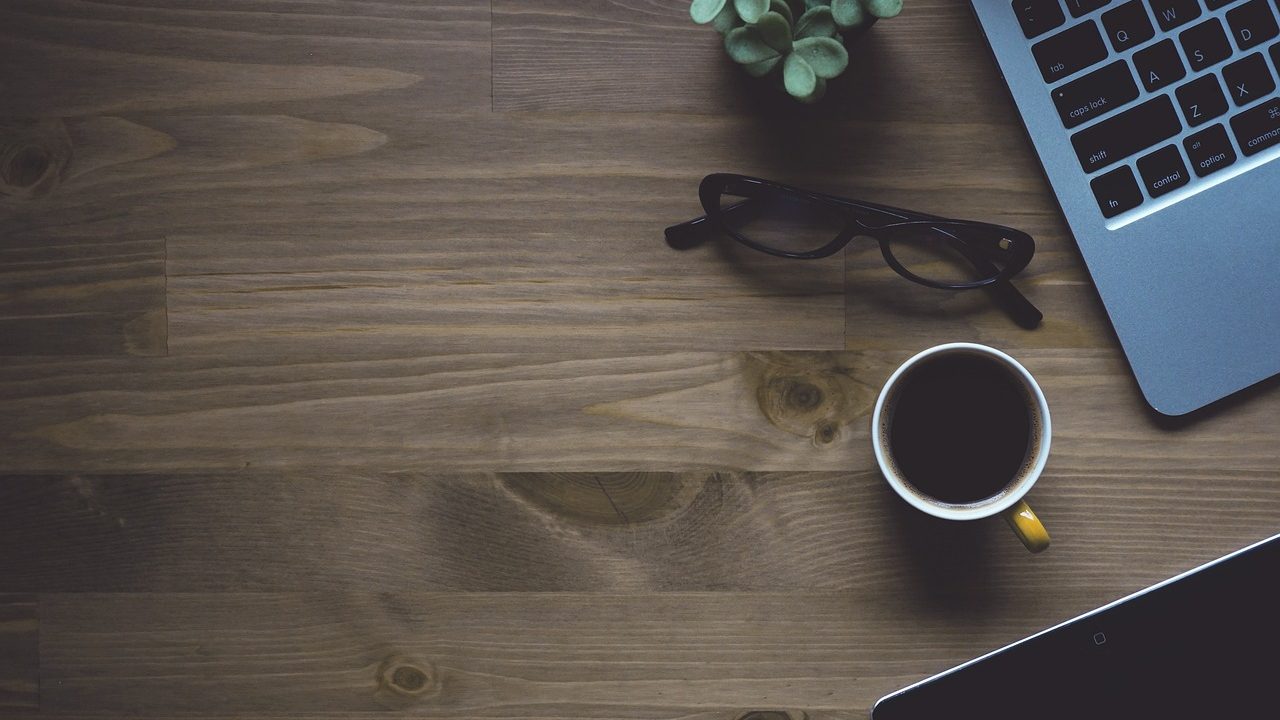 Clean and organized home workspace with an open planner, laptop, and coffee cup on a wooden desk.