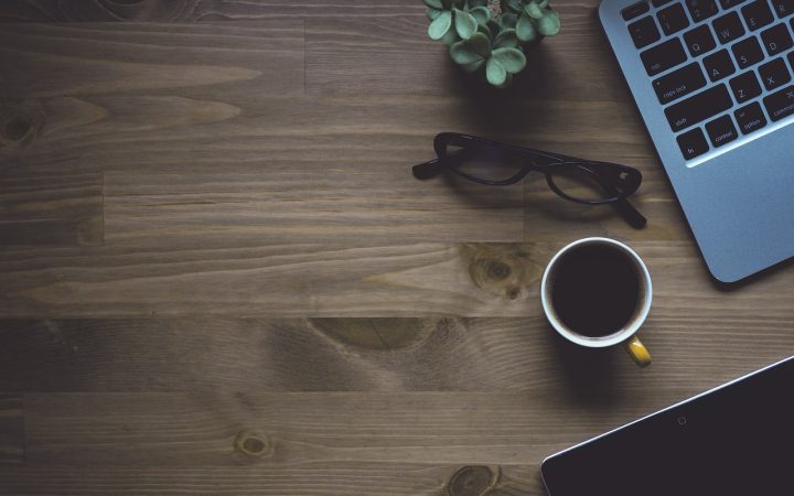 Clean and organized home workspace with an open planner, laptop, and coffee cup on a wooden desk.