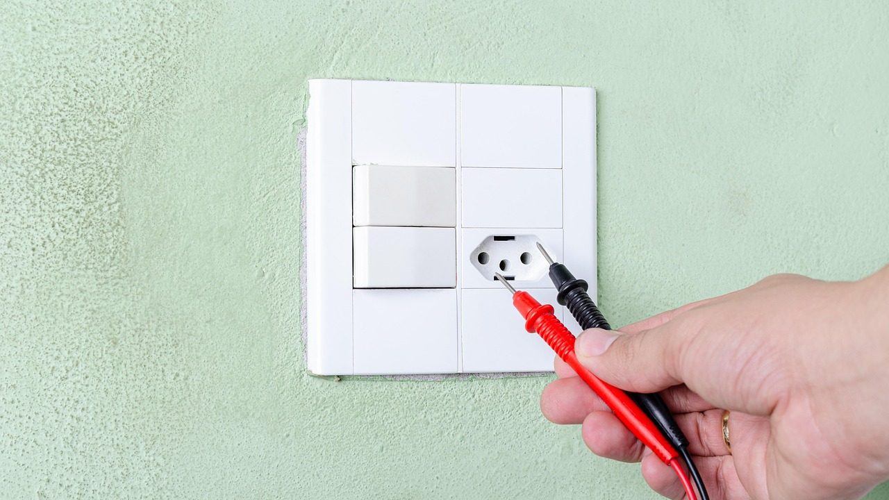 A technician using a multimeter to test the electrical solenoid of a dishwasher water inlet valve behind the lower access kickplate.