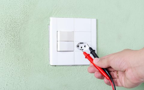 A technician using a multimeter to test the electrical solenoid of a dishwasher water inlet valve behind the lower access kickplate.