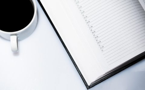 A high school course planning calendar and notebook neatly arranged on a wooden desk in a brightly lit office.