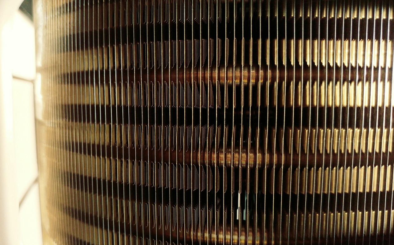 Close-up view of aluminum cooling fins and copper tubing inside a hydronic baseboard heater strip.