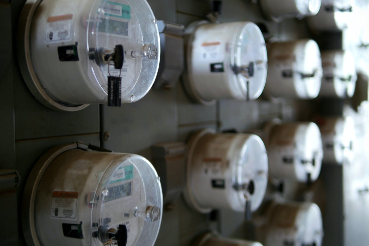 A modern digital smart electric meter mounted on the exterior siding of a suburban house.