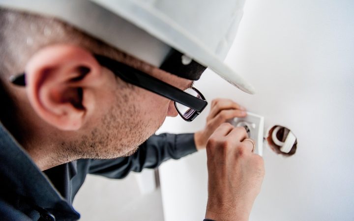 An electrician examining a storm-damaged overhead electric meter socket and service mast on a house exterior.