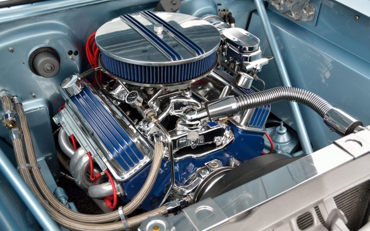 A mechanic inspecting an engine under the hood of a modern car on a lift in a professional repair shop.