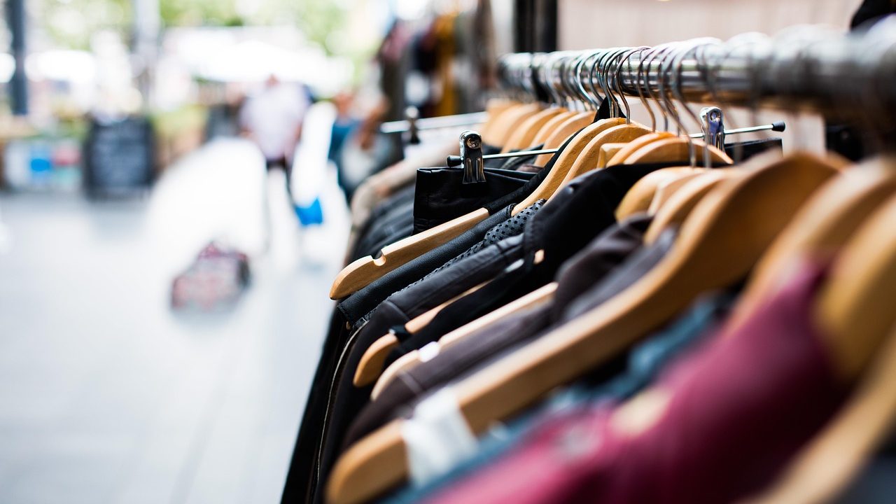 Two racks of apparel inside a well-lit clothing store showing different fabric weights and garment structures.