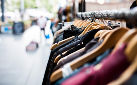Two racks of apparel inside a well-lit clothing store showing different fabric weights and garment structures.
