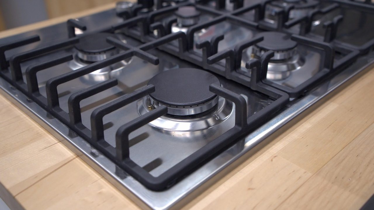 Close-up of a person cleaning a gas stove burner head with a brush