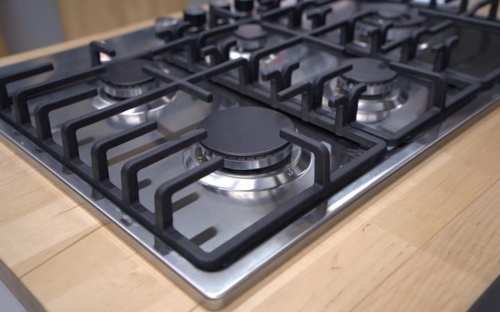 Close-up of a person cleaning a gas stove burner head with a brush