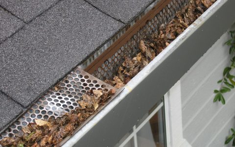 Contractor installing metal gutter protection on a residential roofline.