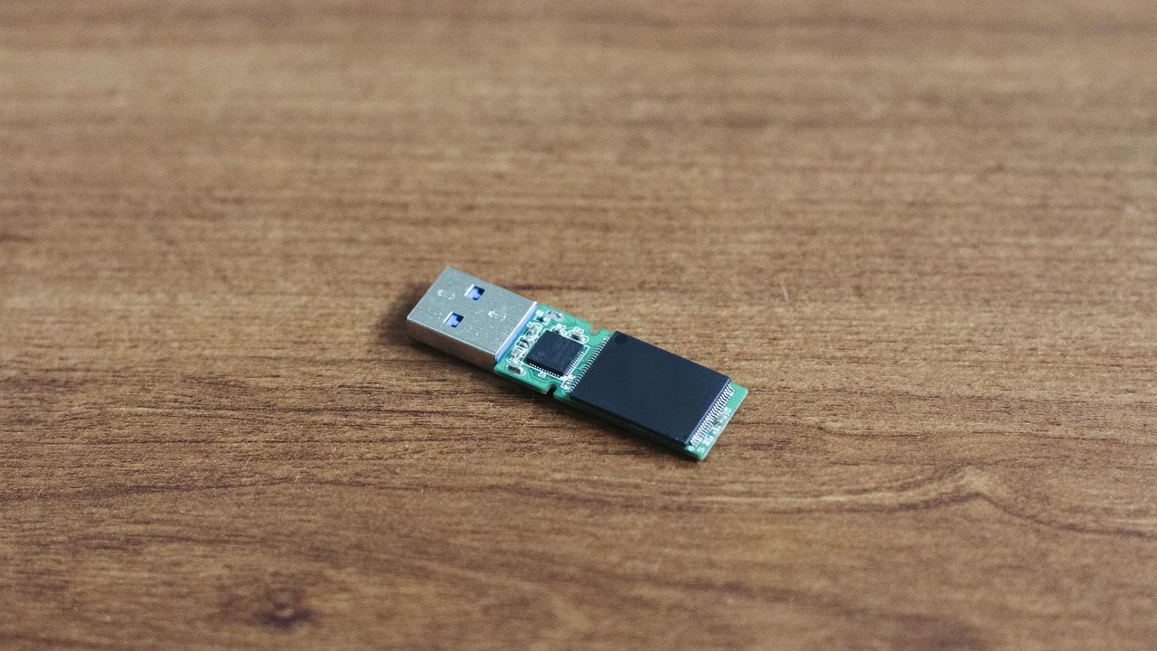 Hardware-encrypted USB drive with physical keypad sitting on a desk near a laptop in a home office.
