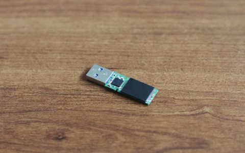 Hardware-encrypted USB drive with physical keypad sitting on a desk near a laptop in a home office.