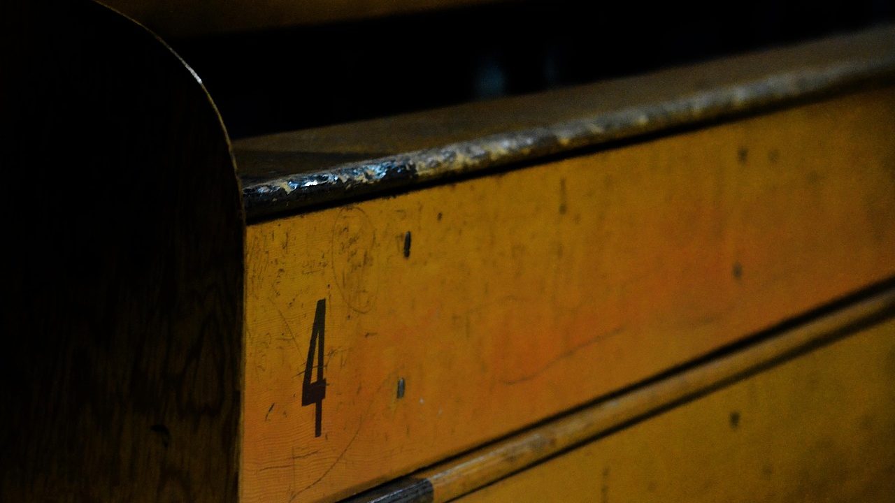 A tryout scoring rubric clipboard sitting on a high school gymnasium bench while cheer athletes practice in the background.