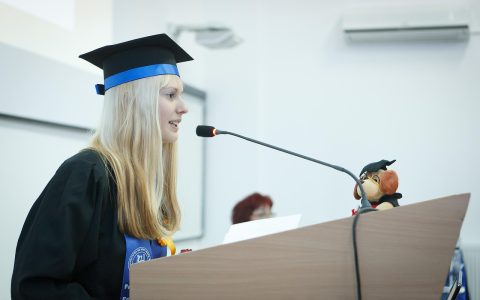 A graduating senior standing at a podium giving a speech during a commencement ceremony.