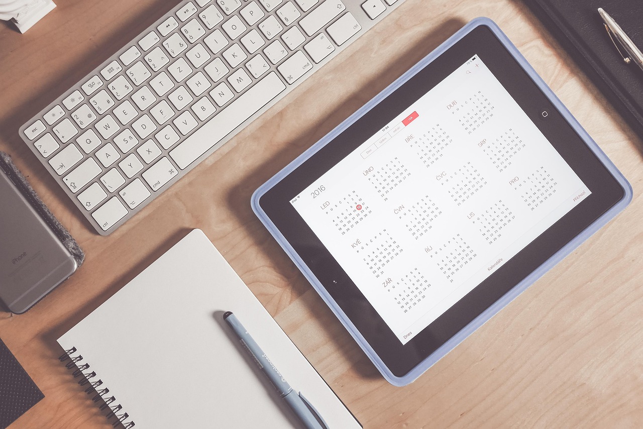 Desk with paper calendar, tablet, and school application checklist.