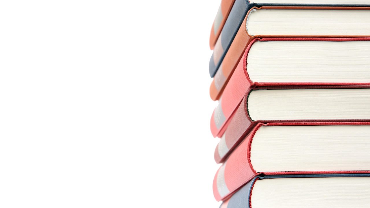 A stacked high school textbook and tablet on a wooden desk.