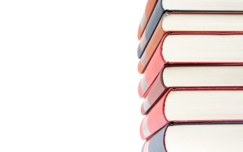 A stacked high school textbook and tablet on a wooden desk.