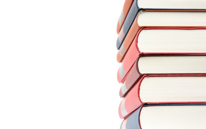 A stacked high school textbook and tablet on a wooden desk.