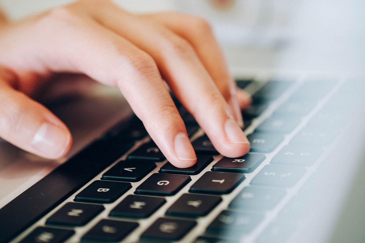 Close up of hands typing on a laptop keyboard while managing online accounts.