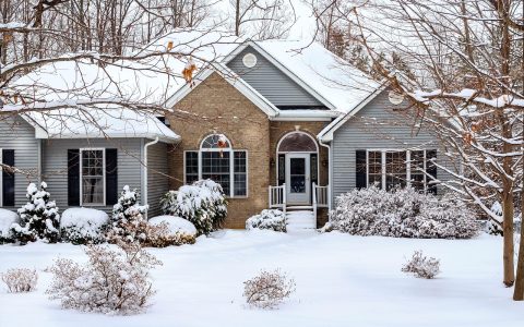 Homeowner washing exterior vinyl siding with a long-handled brush and garden hose