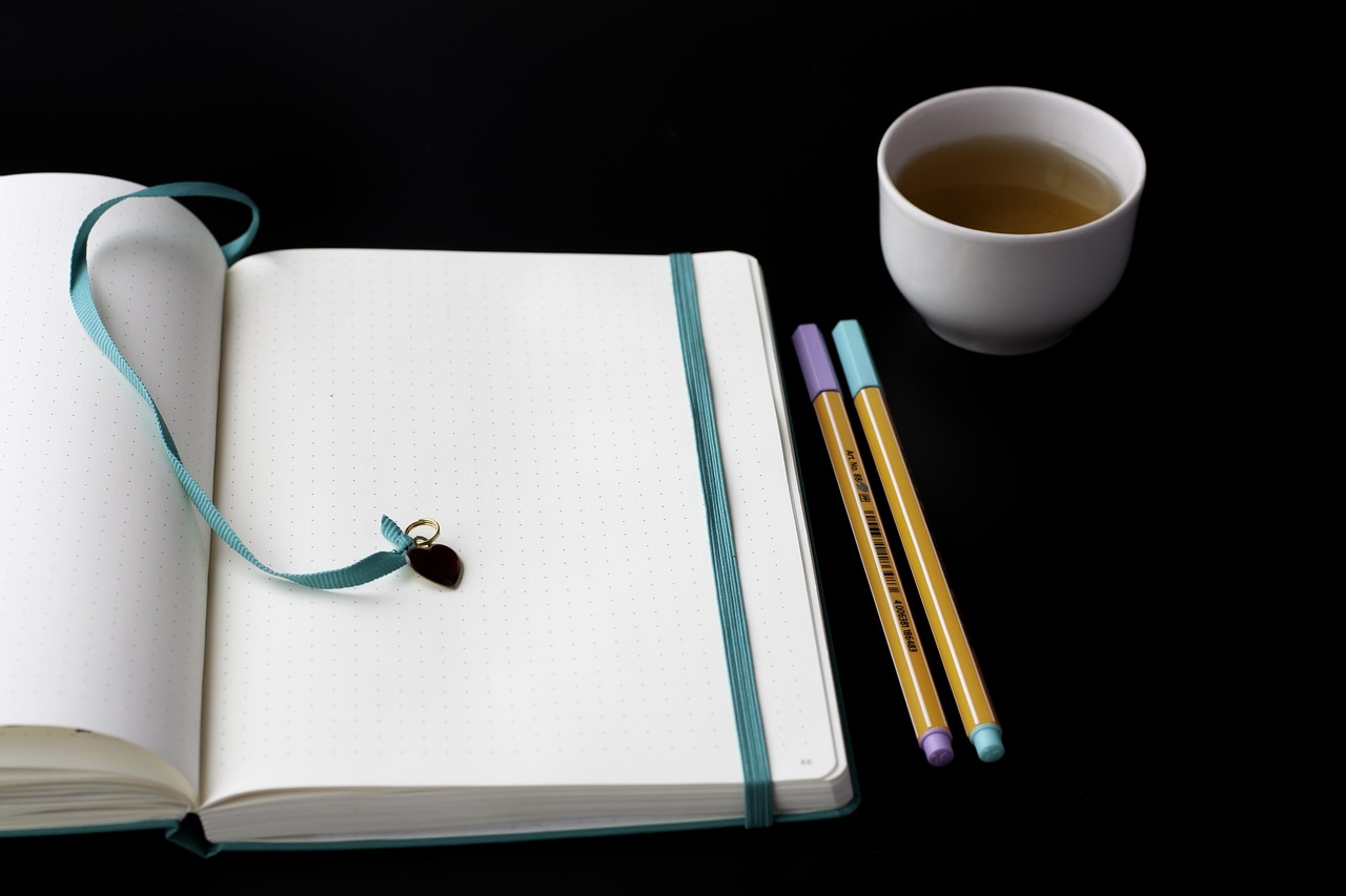 Close-up of a worker typing on a laptop with a handwritten planner and pen resting on the desk.