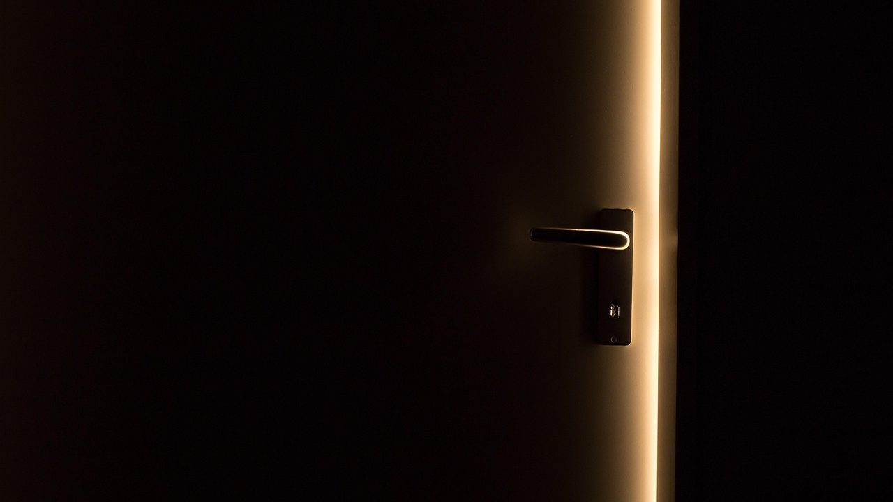 Hand adjusting a brass door hinge with a screwdriver on a wooden interior door frame.
