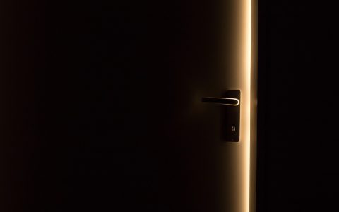 Hand adjusting a brass door hinge with a screwdriver on a wooden interior door frame.