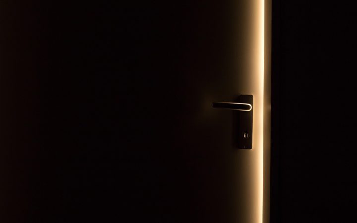 Hand adjusting a brass door hinge with a screwdriver on a wooden interior door frame.