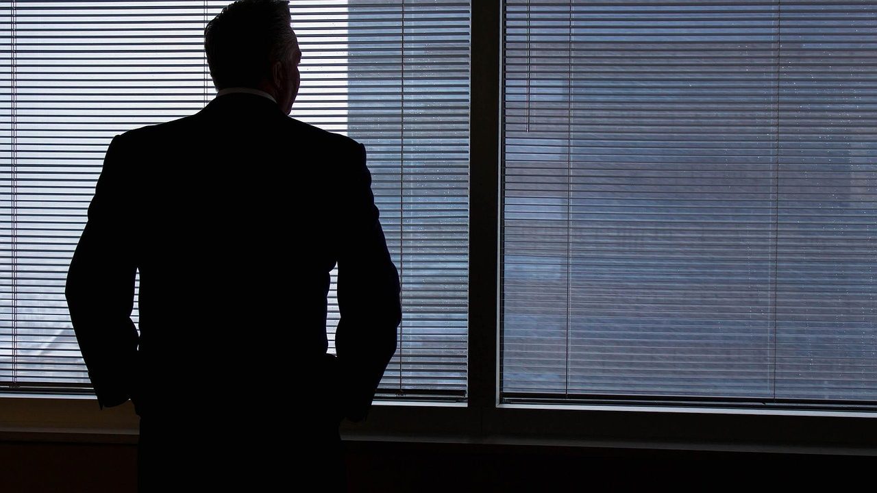 A corporate professional standing by a high-rise office window contemplating a career transition.