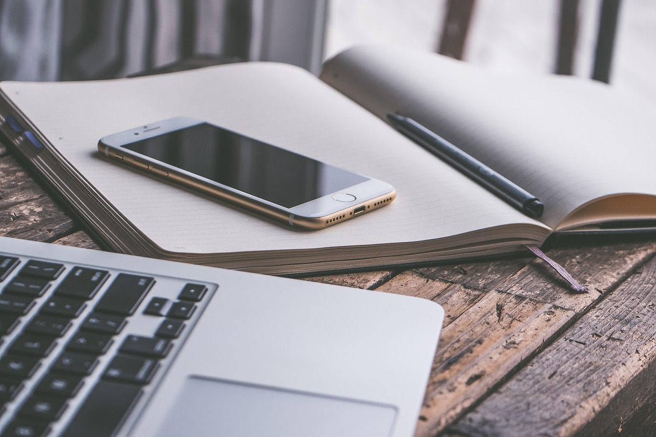 A paper journal and open laptop side-by-side on a wooden desk.
