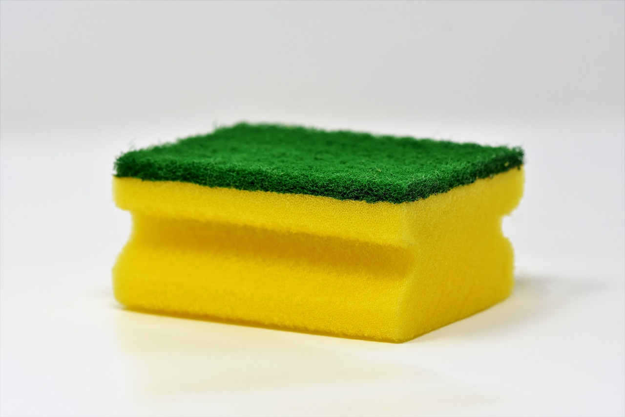 Sanding sponge smoothing joint compound patch on a white drywall wall.