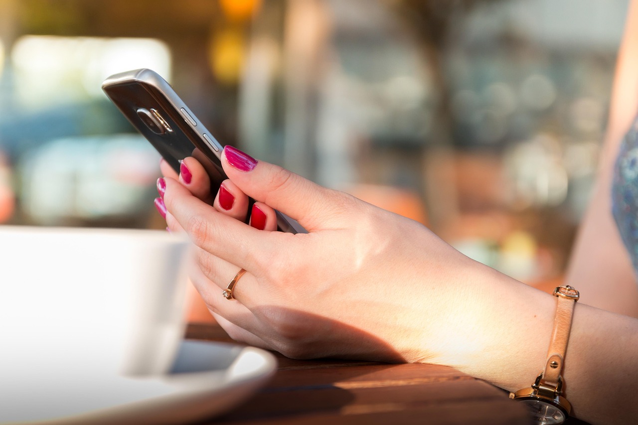 Close-up of a shopper comparing product details on a smartphone beside delivered cardboard boxes