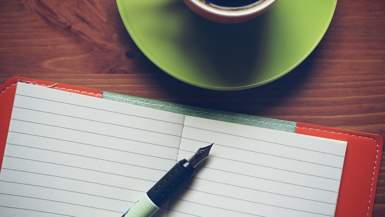 A person writing intentionally in a journal at a minimal wooden desk in a bright, tranquil modern home office.