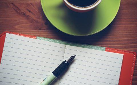 A person writing intentionally in a journal at a minimal wooden desk in a bright, tranquil modern home office.