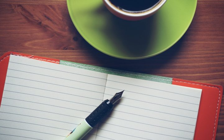 A person writing intentionally in a journal at a minimal wooden desk in a bright, tranquil modern home office.