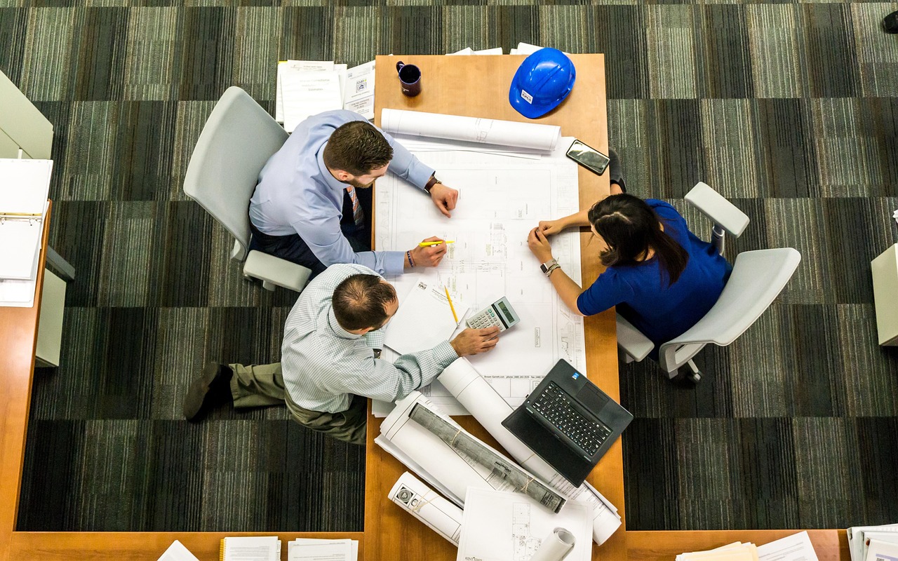 Three business colleagues in discussion around a glass whiteboard during a strategic calibration session.